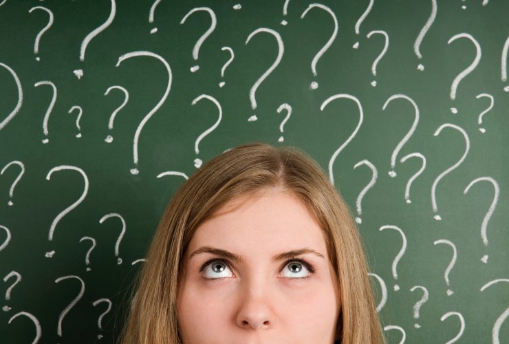 A woman in front of a chalkboard with question marks drawn all over it.